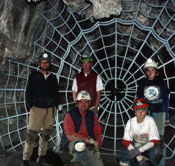 The Crystal Cave Gate resembles a spiderweb. Multiple cavers stand proudly in front of the beautiful gate.