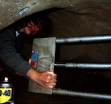 A caver performs routine maintenance on a cave gate.